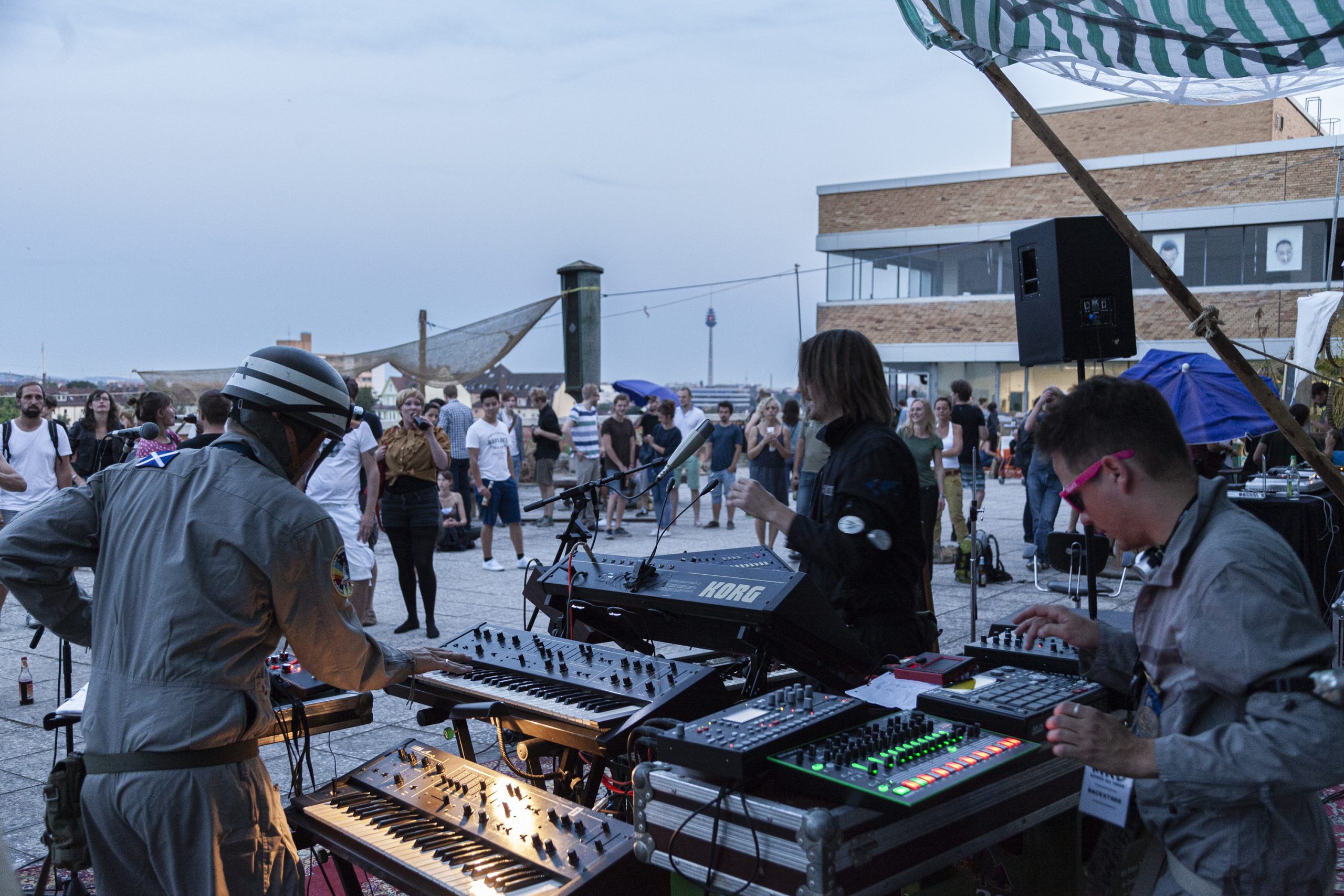 Ein Fest mit DJs unter freiem Himmel mit Personen im Hintergrund und einem Teil des Gebäudes The Q rechts im Anschnit.